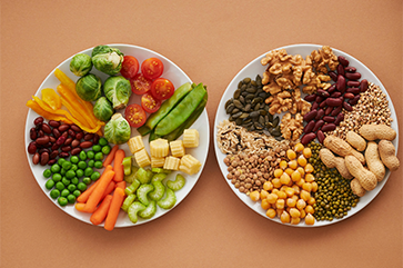 Two plates display vegetables and halved tomatoes, nuts and legumes including chickpeas and walnuts
