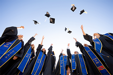 Eight students in graduation robes and blue Class of 2025 stoles tossing their mortarboards into the air