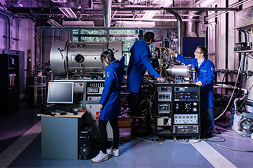 Scientists in blue coats working with machinery in a lab