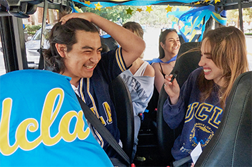 Four students smile as they sit in a golf cart with UCLA script logo covering the front seat