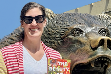 Lauren Stienstra posing with her book, "The Beauty of The End," with the Bruin Bear Statue in the background.