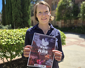 Lena Trüper standing outdoors holding a flyer for "Wake the Flies," a documentary she produced