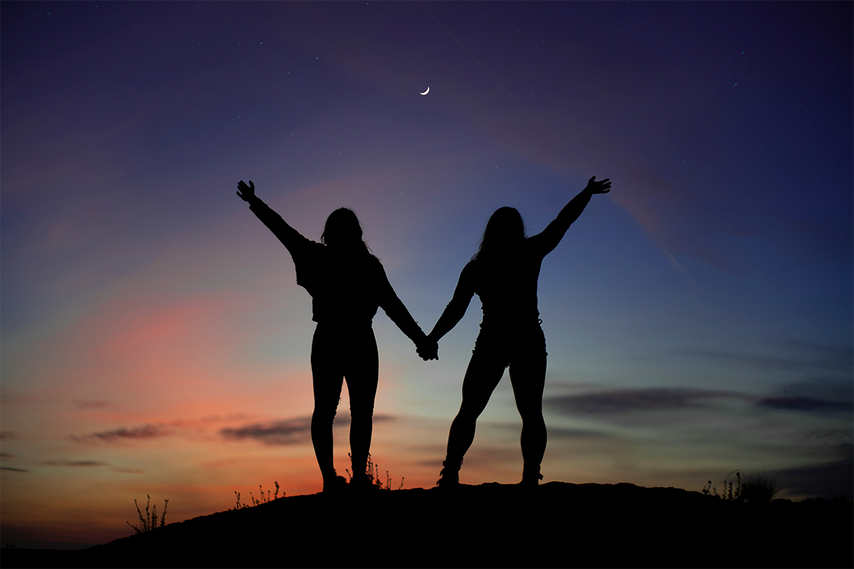 The silhouettes of two girls holding hands against a dusk sky. 