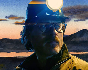 Jonathan Webb, a 2025 Pritzker nominee and Co-founder of The Nuclear Company, wears a hard hat and glasses while looking into the distance. A soft watercolor-style mountain landscape appears behind him.