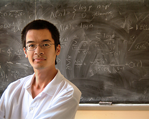 Terence-Tao-363-241 Terence Tao in a white polo shirt against a chalk board with equations.