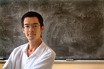 Terence Tao in a white polo shirt against a chalk board with equations.