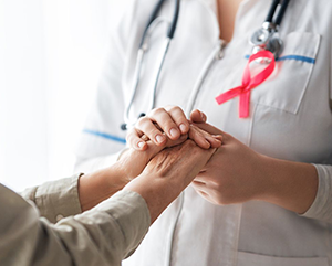iStock–363-241 A patient, left, and medical care provider holding hands; provider has a pink breast cancer ribbon on her lapel