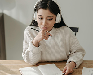 pexels-pavel-danilyuk-363-241 Young woman wearing white headphones studies with head propped on hand