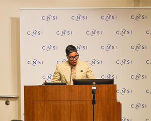 Ivy McGregor speaking at a podium in front of a CNSI step-and-repeat banner