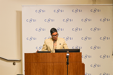 Ivy McGregor speaking at a podium in front of a CNSI step-and-repeat banner
