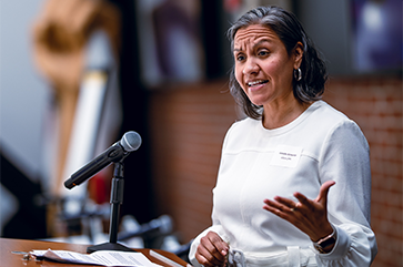Amada Armenta, in white, gestures with her left hand as she speaks at a podium