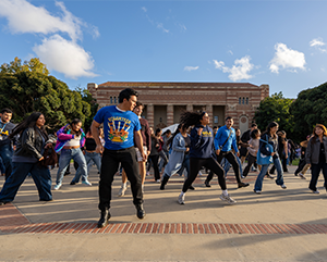 A large group of students dance in Wilson Plaza against a dramatic sky at the 2025 ‘Latinx Success Center Welcome.’