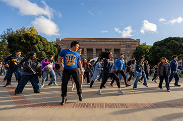 A large group of students dance in Wilson Plaza against a dramatic sky at the 2025 ‘Latinx Success Center Welcome.’
