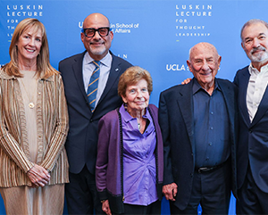 Five smiling people standing in front of Luskin Lecture for Thought Leadership step-and-repeat banner