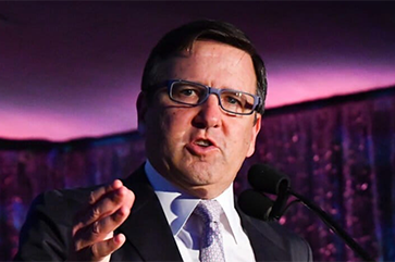 Tony Pritzker speaking at the UCLA Institute of the Environment and Sustainability (IoES) gala in front of a white podium.