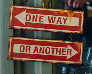 Two red signs with white arrows reading ‘one way’ or ‘another’ hanging from a metal pole