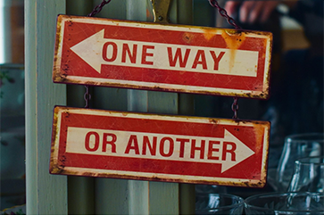 Two red signs with white arrows reading ‘one way’ or ‘another’ hanging from a metal pole