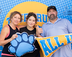 Student mother father posing in front of sign – 363 – 241 A female student posing with her mother and father.