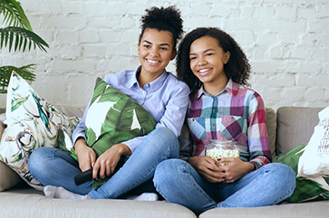 Two teens watch TV and eat popcorn