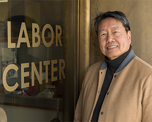 Kent Wong, in tan and gray jacket, standing next to glass door with Labor Center printed on it