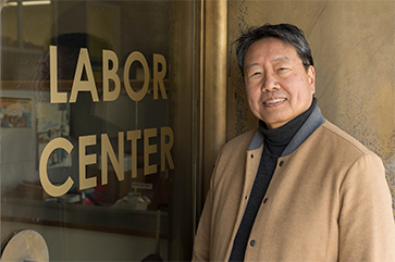 Kent Wong, in tan and gray jacket, standing next to glass door with Labor Center printed on it