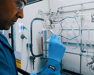 Neil Garg in a blue lab coat writing on a clear board.