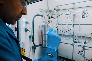 Neil Garg in a blue lab coat writing on a clear board.