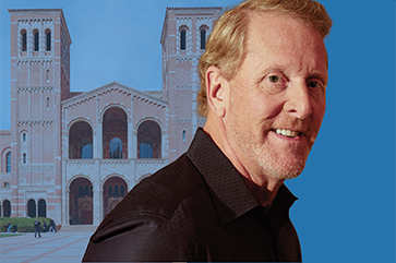 Barry Eggers in front of UCLA’s Royce Hall. The iconic twin-towered building features Romanesque architecture with arched windows and decorative brickwork. The right side of the background is replaced with a solid blue color, creating visual contrast.