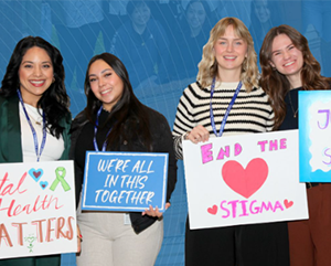 Four women holding signs against a blue background