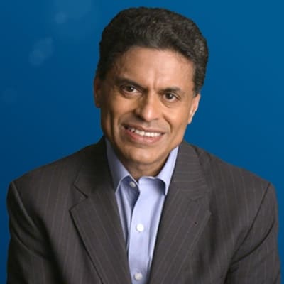 A man with dark hair, wearing a pinstripe suit and light blue shirt, smiles in front of a blue background.