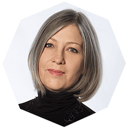 A woman with straight, shoulder-length gray hair and blue eyes, wearing a black turtleneck top, poses in front of a light background.