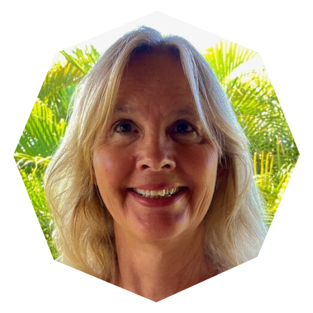 A woman with long, blonde hair smiles at the camera. She is outdoors with green palm trees and a bright sky in the background. The photo has a hexagonal border.