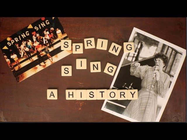 Two photos—one of a group performing on stage under a “Spring Sing” sign, and one of a woman singing—are arranged around Scrabble tiles spelling “Spring Sing A History” on a wooden surface.