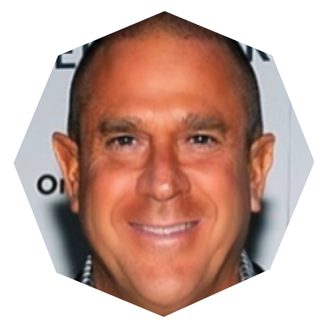 A man with a shaved head and broad smile is photographed in front of a partially visible backdrop, shown within an octagonal frame.