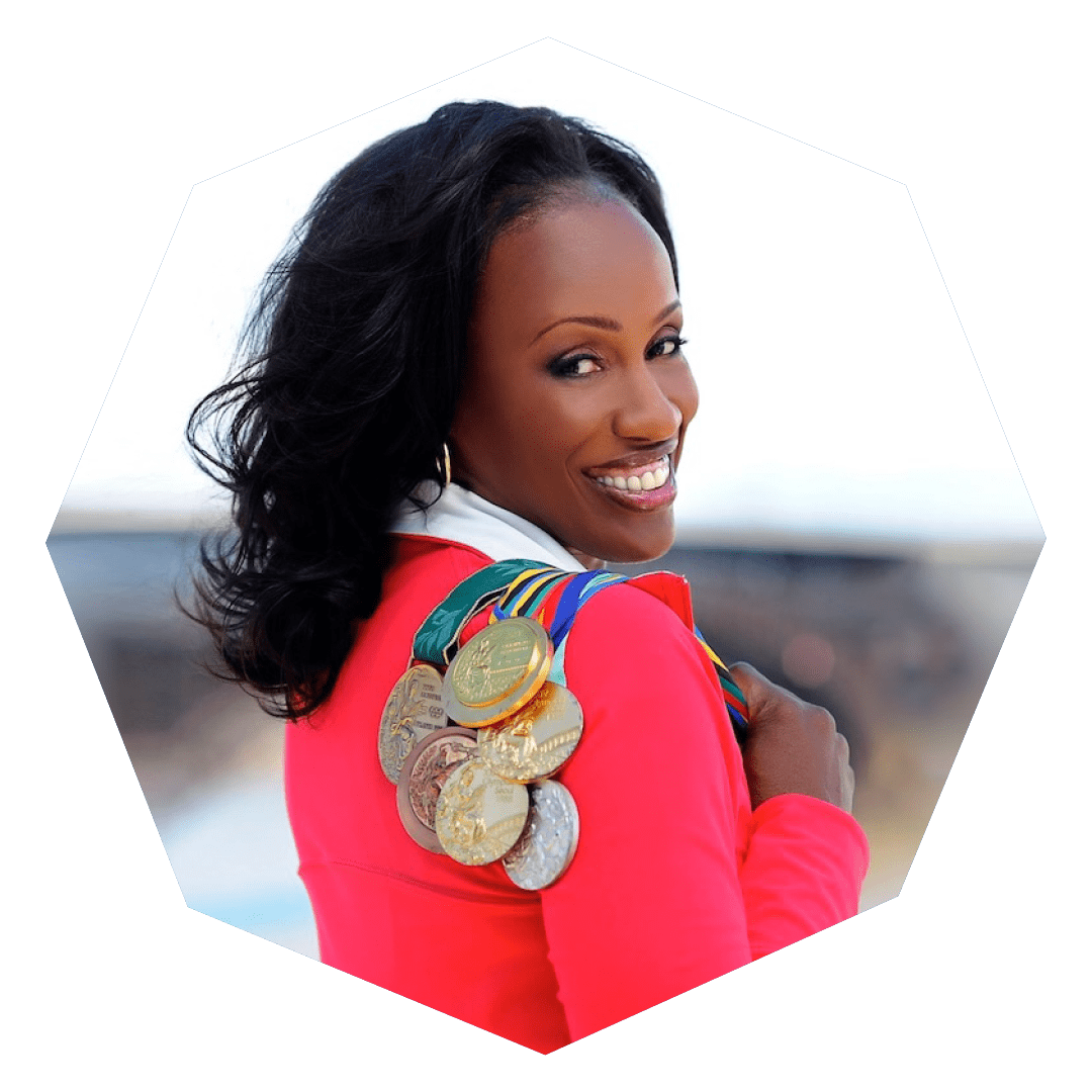 A woman in a bright jacket smiles over her shoulder, holding several medals draped over her arm, with an outdoor background softly blurred behind her.