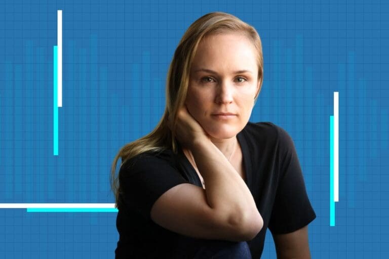A woman with blonde hair and a black shirt rests her head on her hand, sitting in front of a blue grid background with white and turquoise vertical graph lines.