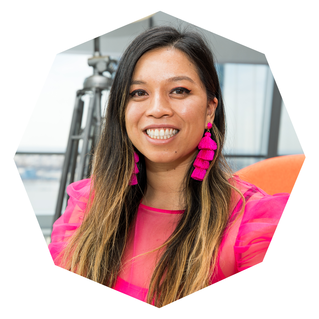 Jennifer Lee sits on an orange couch wearing a pink dress and pink earrings