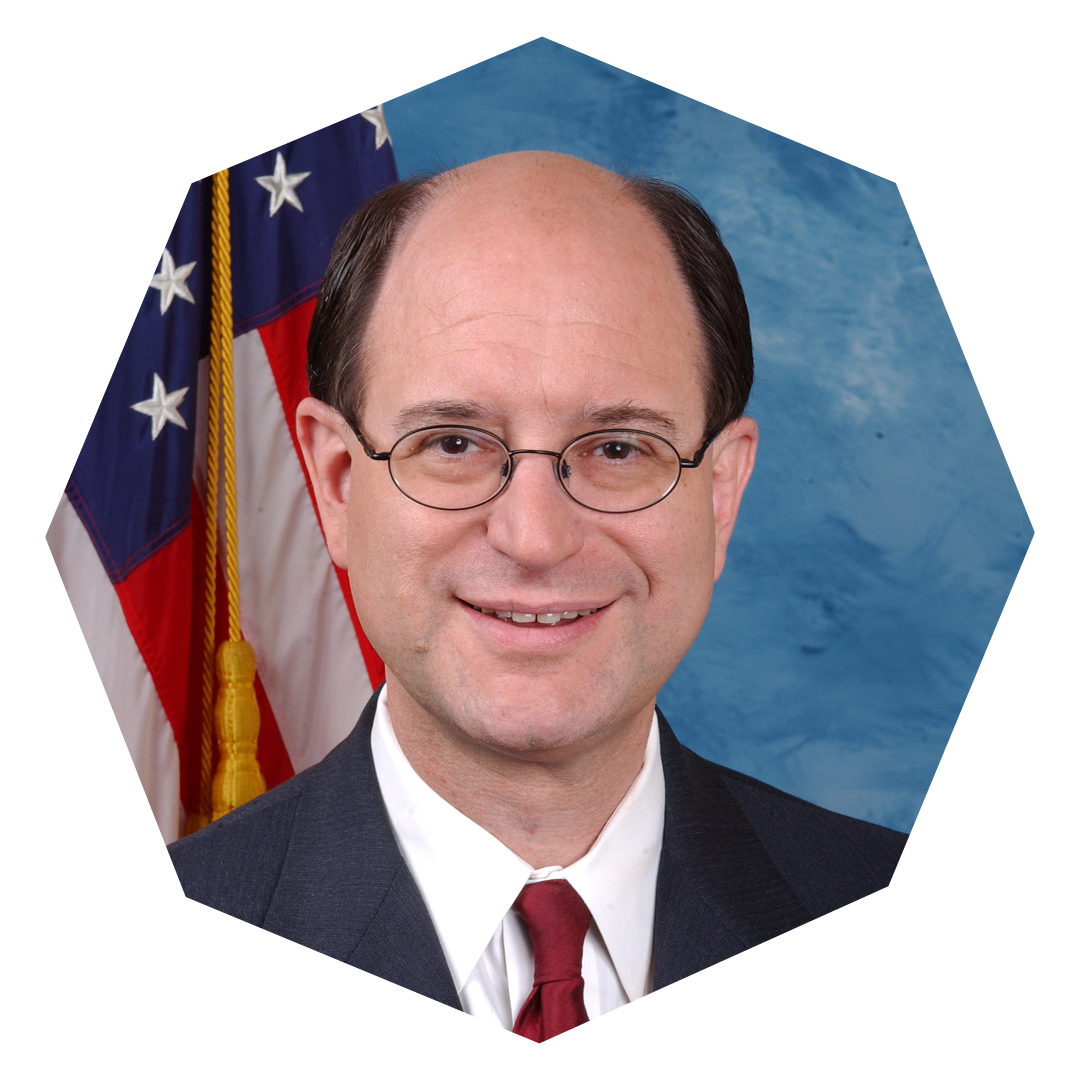 Brad Sherman in a blue suit, a white shirt and a red tie. The photo is framed in an eight-sided molecule.
